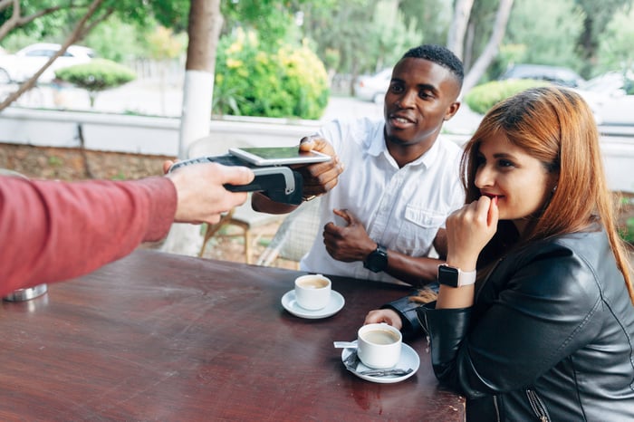 A couple making a contactless payment with their smartphone while seated at a cafe. 