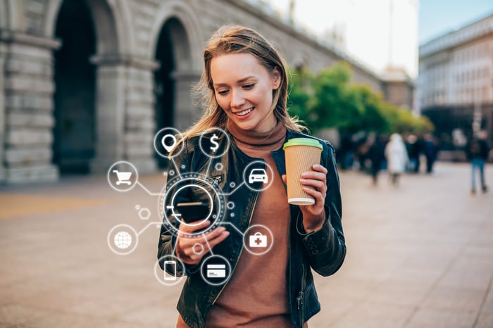 Person standing outdoors looks at mobile device as icons of digital activities float around the phone.