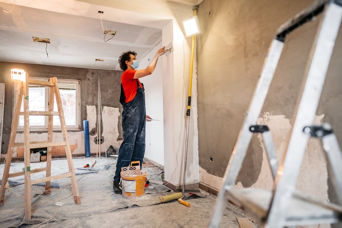 A masked person plastering a wall.