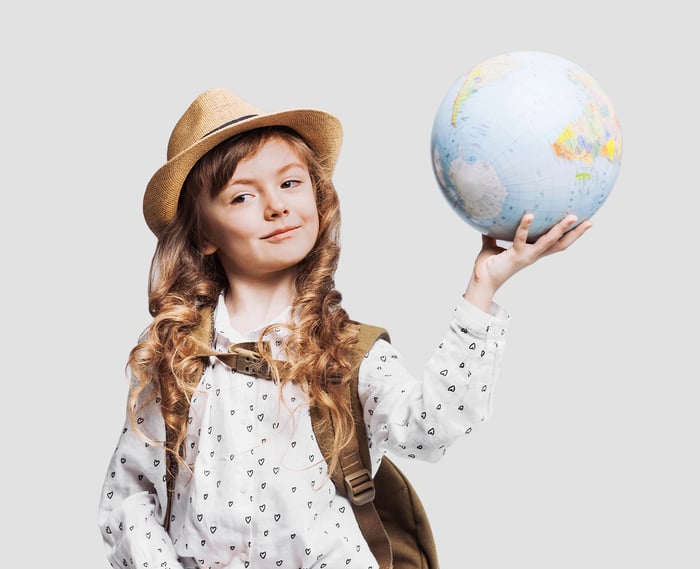 A young person in a hat is holding a globe and smiling. 