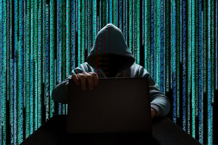 Shadowy hacker at a laptop against a background of streaming computer code.