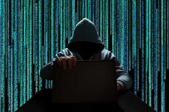 Shadowy hacker at a laptop against a background of streaming computer code.