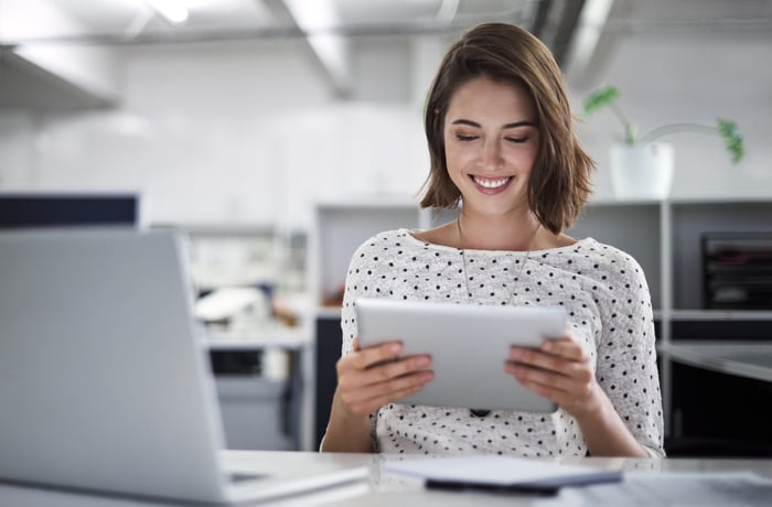 A person in an office holding a tablet and smiling.