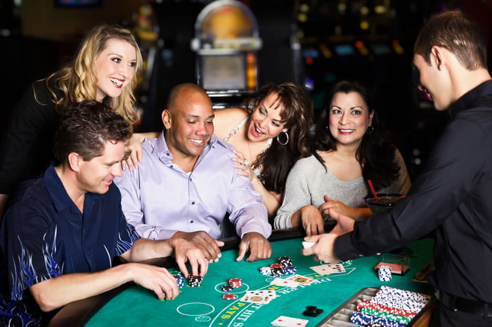 Five people at a casino table with an employee dealing cards.