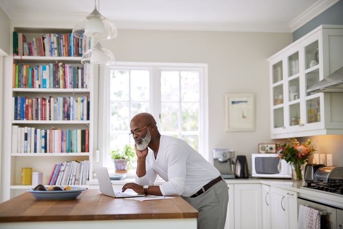 A person leaning over a laptop at a kitchen counter.