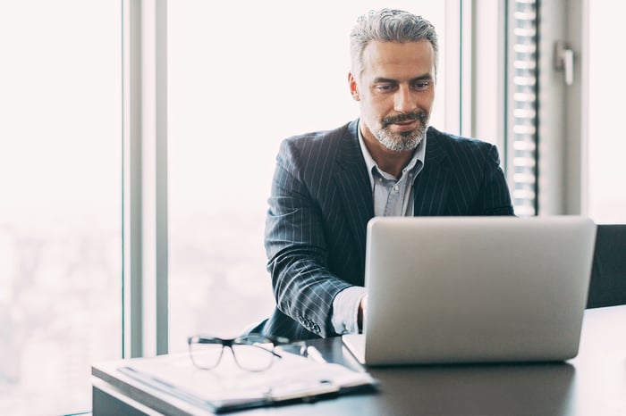 A smiling professionally dressed person at a laptop.