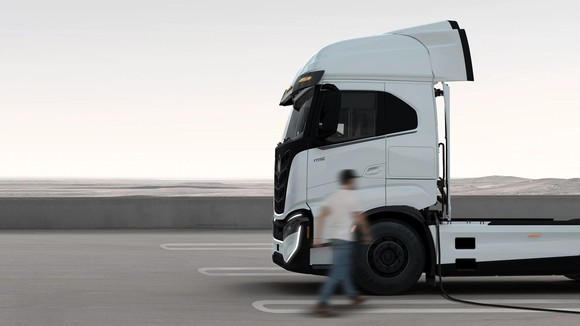 Person walking by a Nikola truck in a desert landscape.