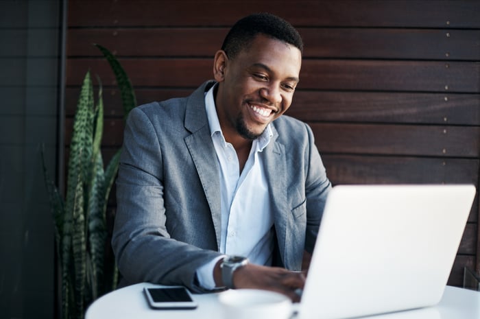 A smiling professionally dressed person at a laptop.