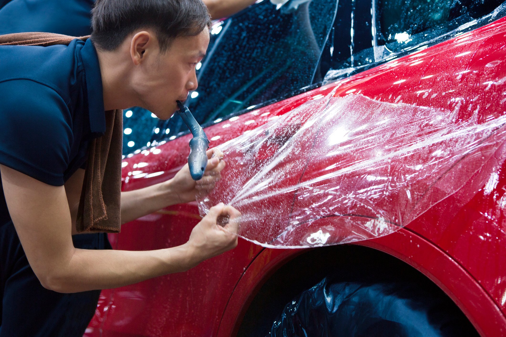 A person of Asian ethinicity working on a car at a workshop.