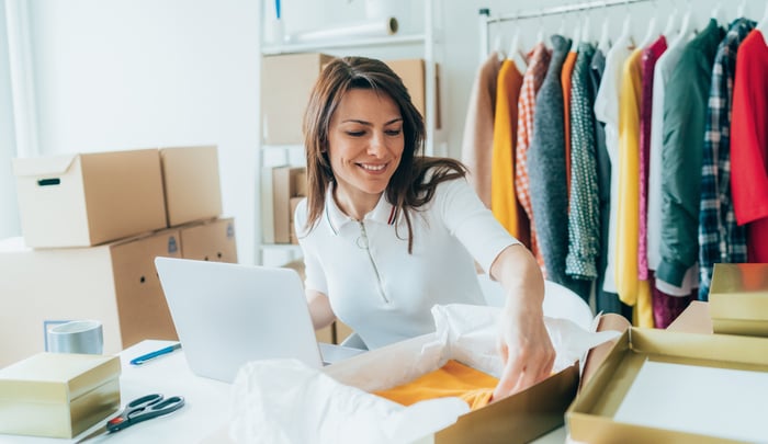 Smiling small business owner packing a customer order into a shipping box.