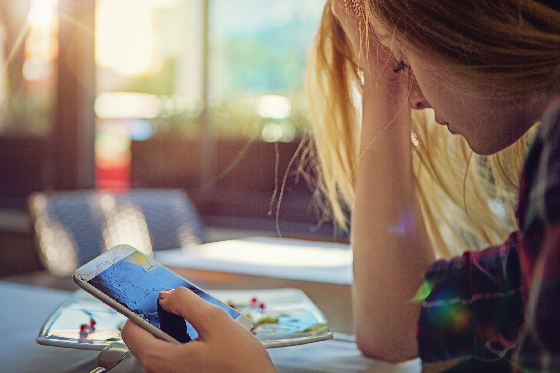 woman looks at broken cell phone with disappointment getty