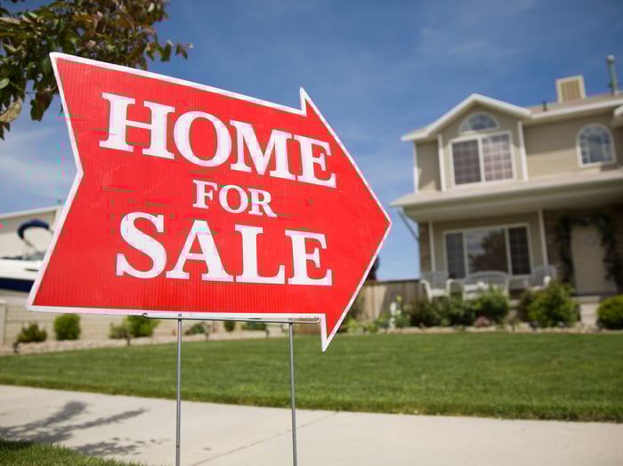 A house with a sign pointing toward it saying home for sale.