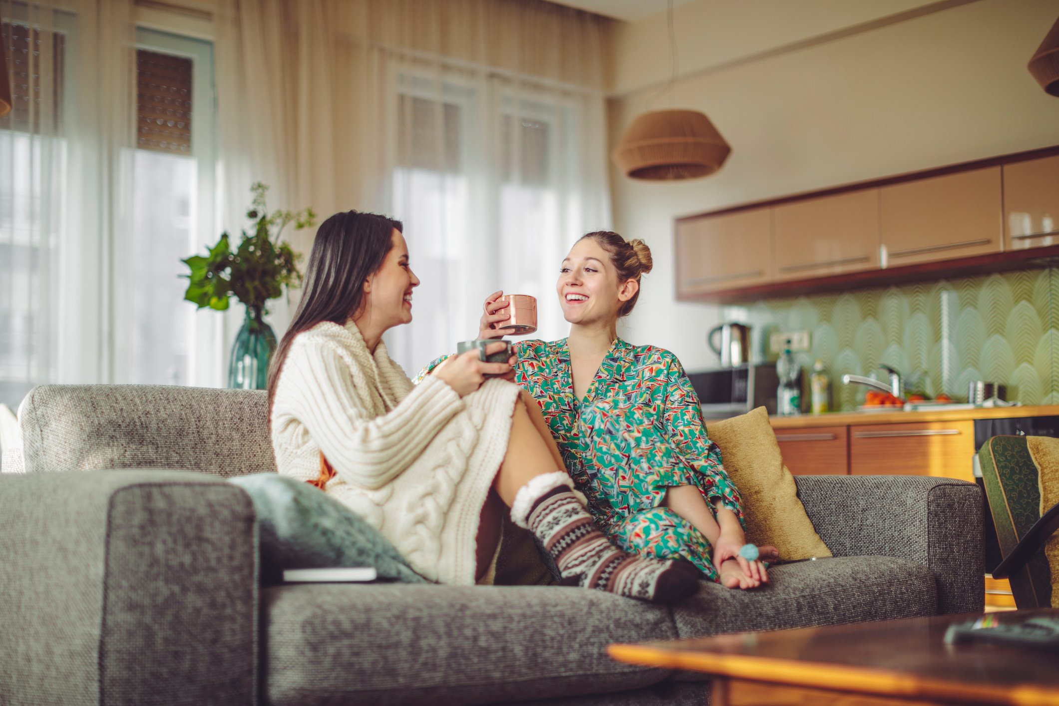 Two people sitting on a couch drinking coffee in pajamas