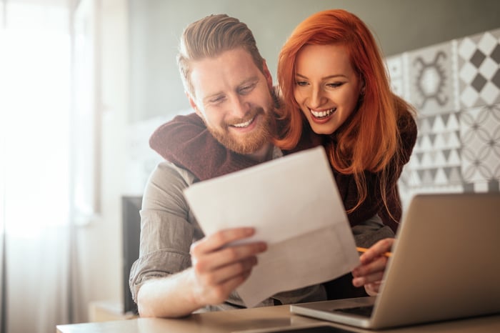 Two investors smile as they look at a document in front of a computer in a home setting.