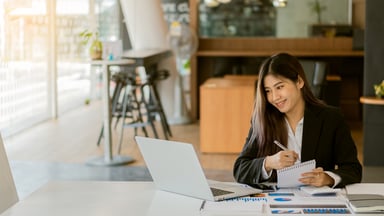 business person takes notes from computer and papers