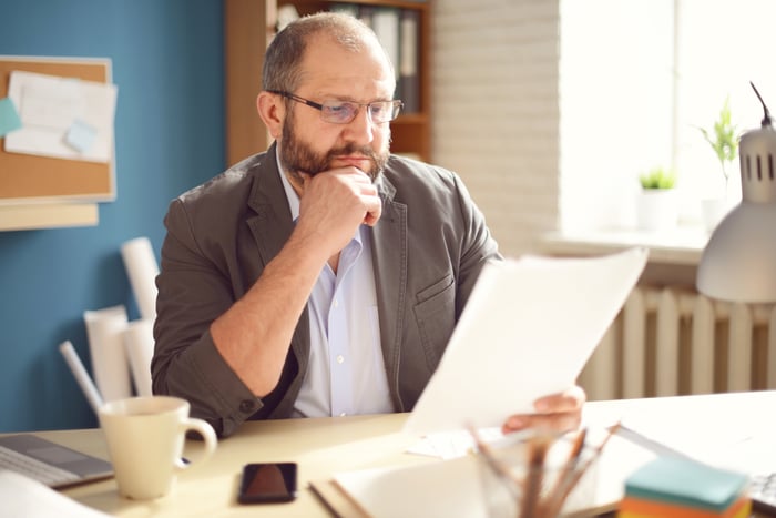 A somewhat older person with a serious expression is examining a document.