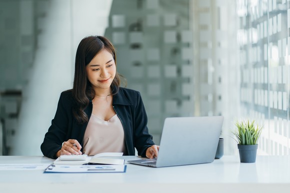 A smiling woman works on a laptop.