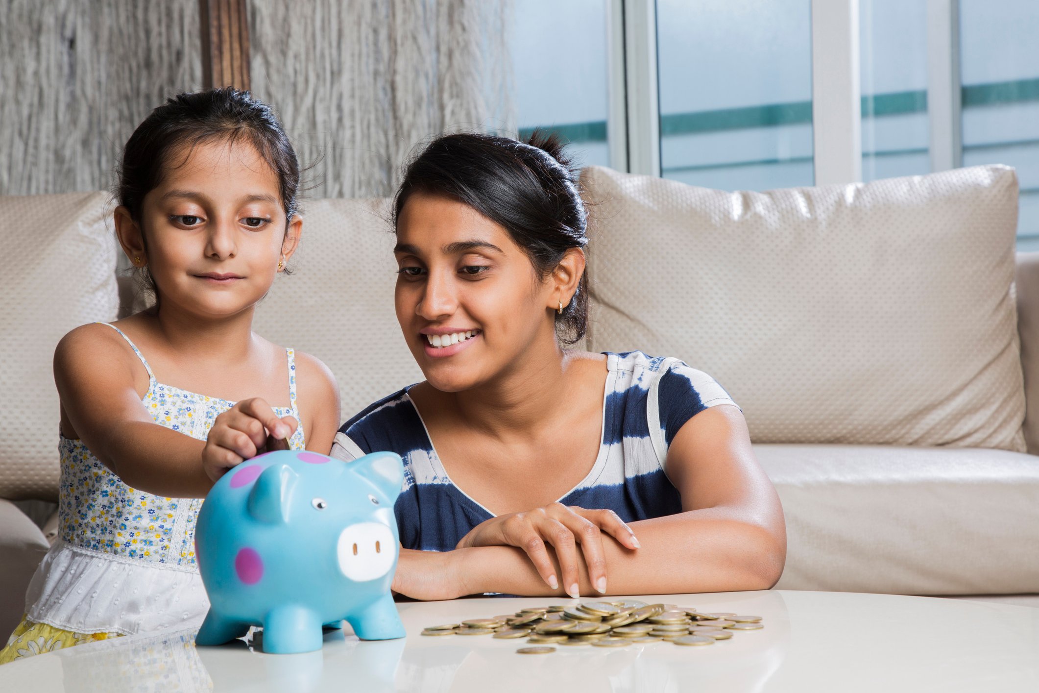 A person and a child putting coins in a piggy bank.