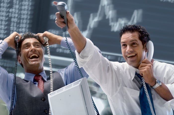 Two excited people wearing business attire hold multiple corded phones.