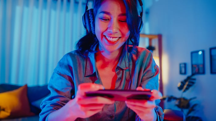 A smiling gamer playing on their smartphone, with headphones on.