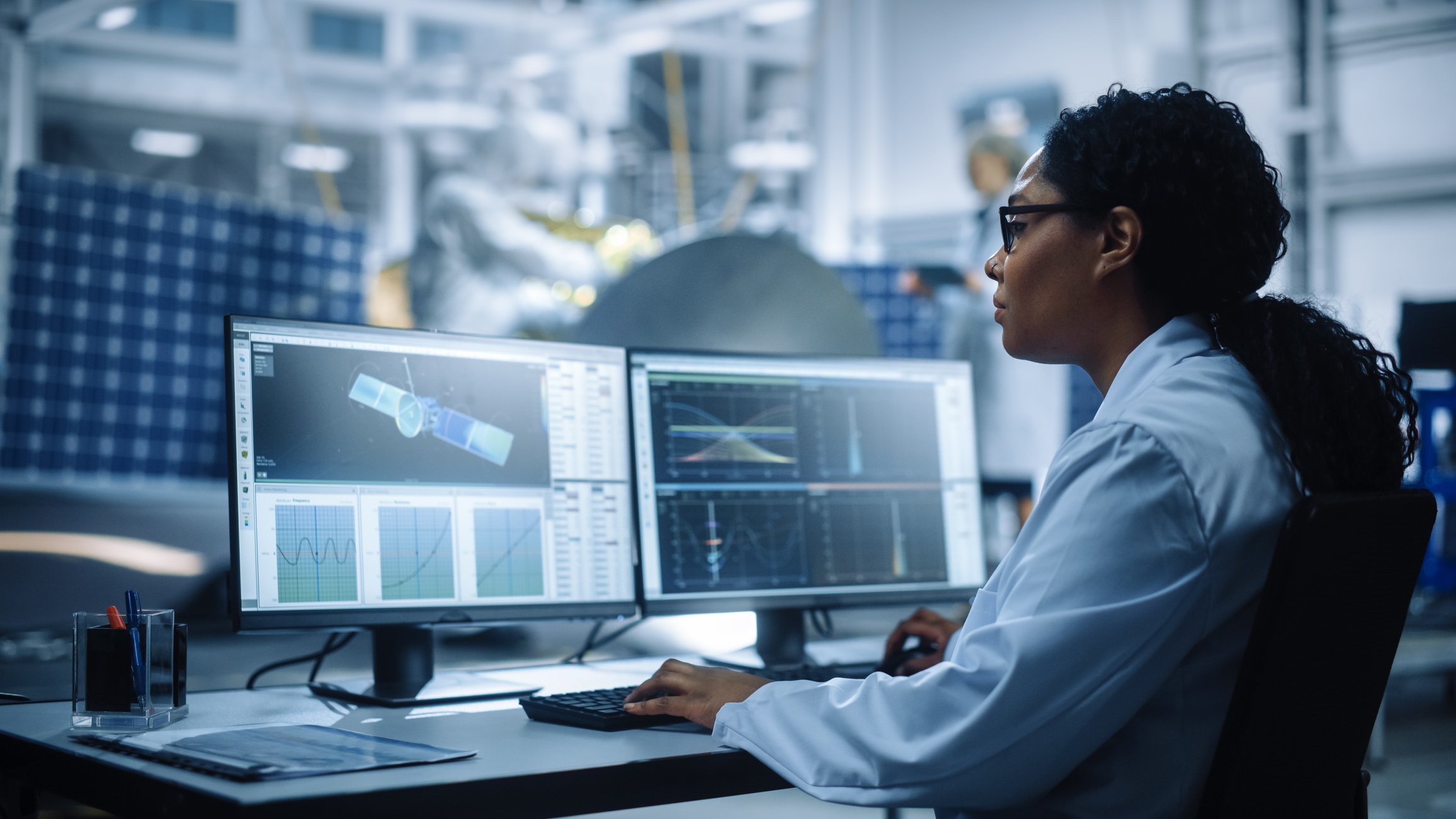 A female engineer analyzes a satellite on a computer.