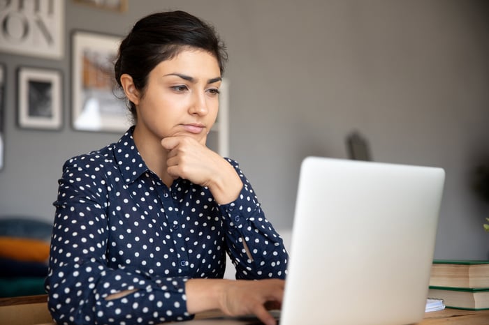 Serious person with hand on chin looking at laptop.