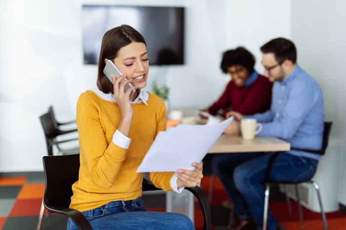 Person sitting in an office talks on mobile phone while looking at papers.