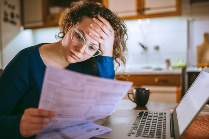 Overwhelmed person with hand on head looking at document.