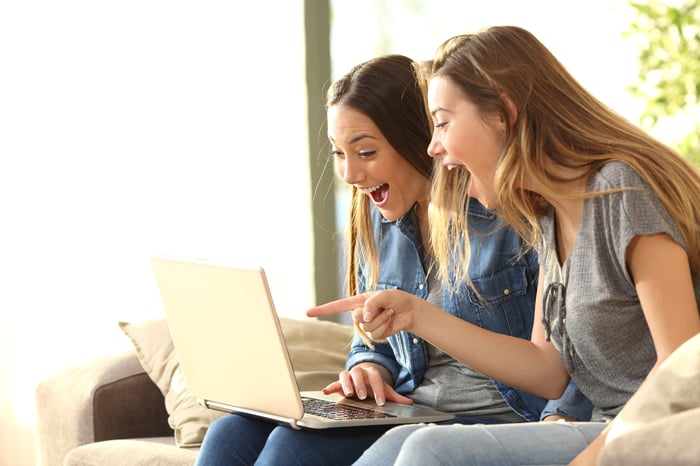 Two people sitting on a couch looking at a laptop.
