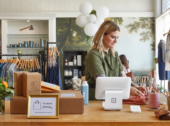 A Square point of sale terminal sits on a counter next to a cashier checking out a customer.