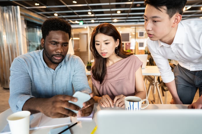 Three people look at a phone