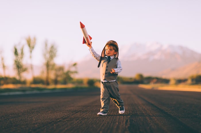 Little boy in an aviator's cap holding a toy rocket high.