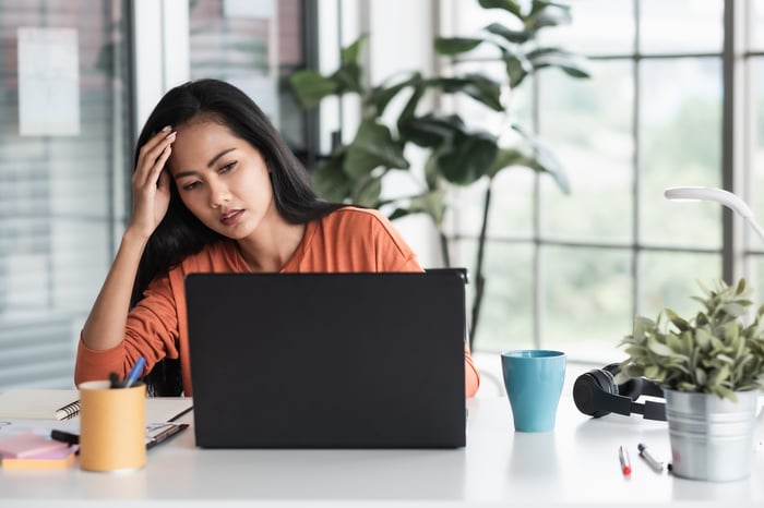 Stressed person with hand on head looking at laptop.