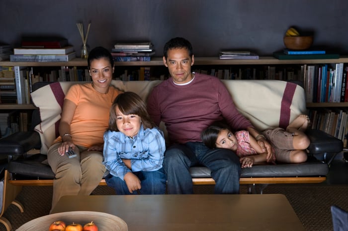 Young family with children huddled together on the couch watching TV.