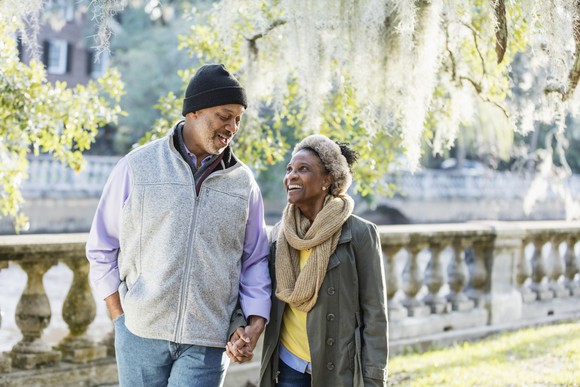Two older people walking in a park holding hands.