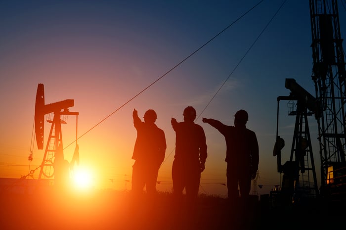 People near an oil well with the sun rising in the background.