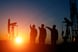 People near an oil well with the sun rising in the background.