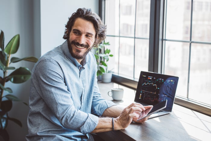 Guy smiling with stock chart on laptop in background.