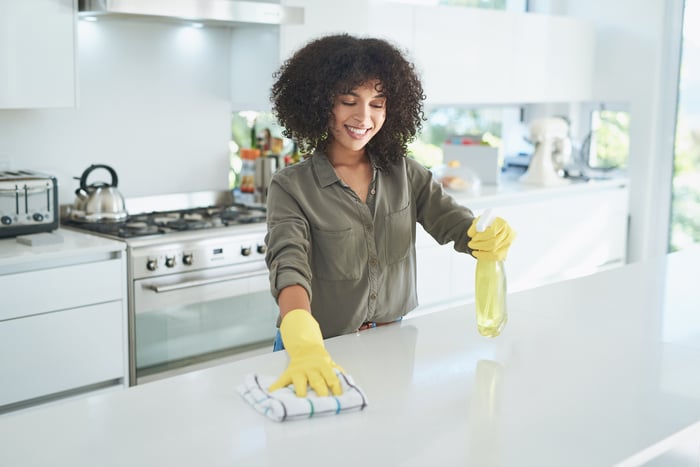 A person using cleaning products and a hand towel to disinfect a kitchen counter. 