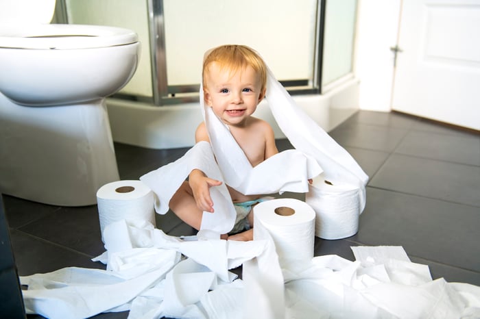 A small child sitting in a pile of toilet paper.