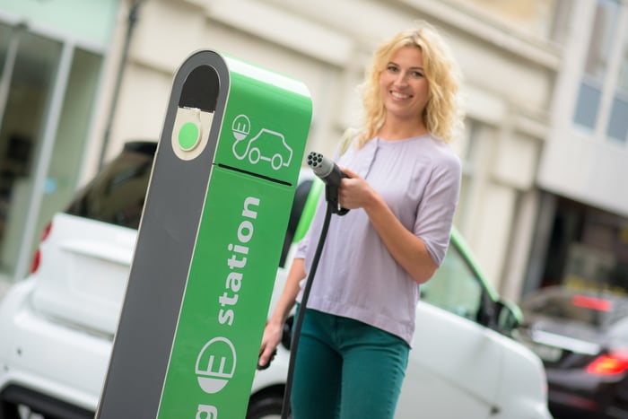 A person holding an electric car charger at a charging station.