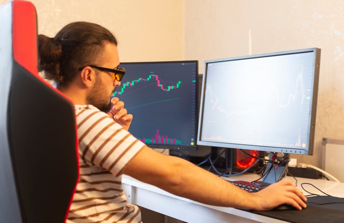 An investor curiously looking at charts on a dual monitor computer.