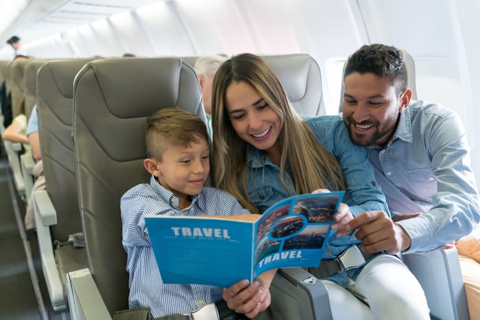 Three passengers on a flight smiling and looking at a brochure together