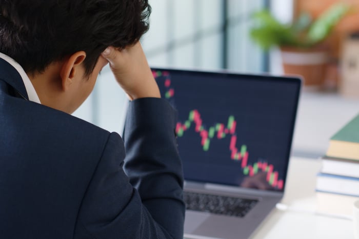 A frustrated business person looks at a falling investment chart on a laptop.