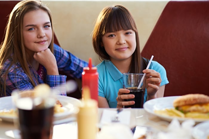 Two children with food and soda at a table.