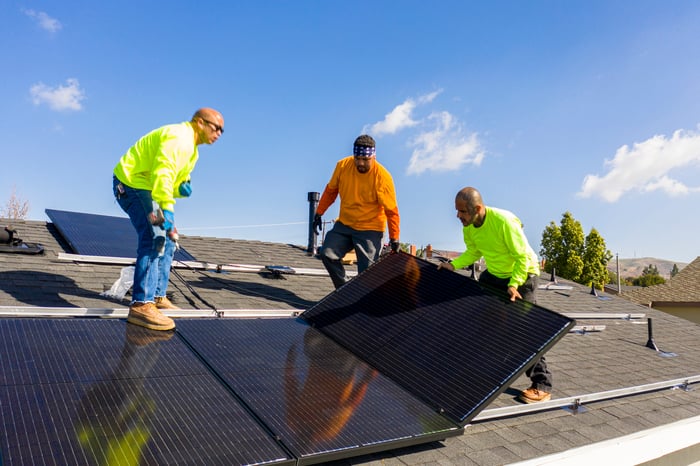 Workers install solar panels on the roof of a home.