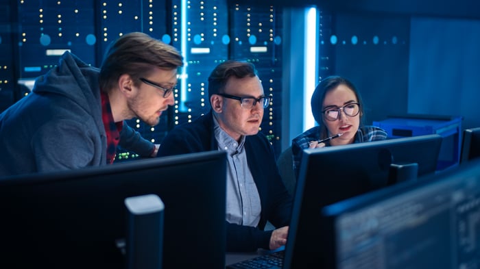 Three people looking at a computer with servers behind them.