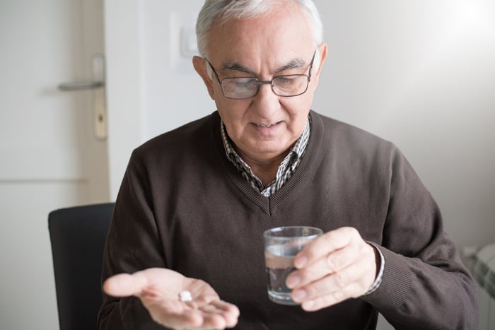 A person holding pills in one hand and a glass in the other.