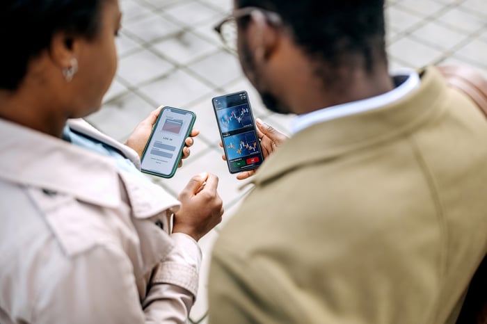 Two people looking at stock charts on their cellphones.