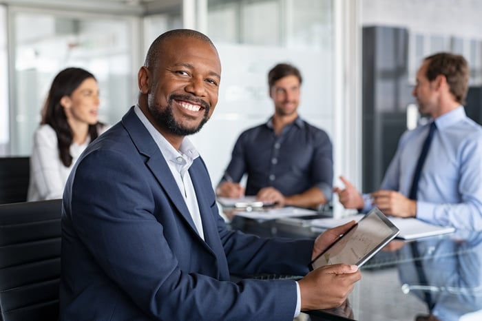 Person sitting at an office table smiling at tablet.